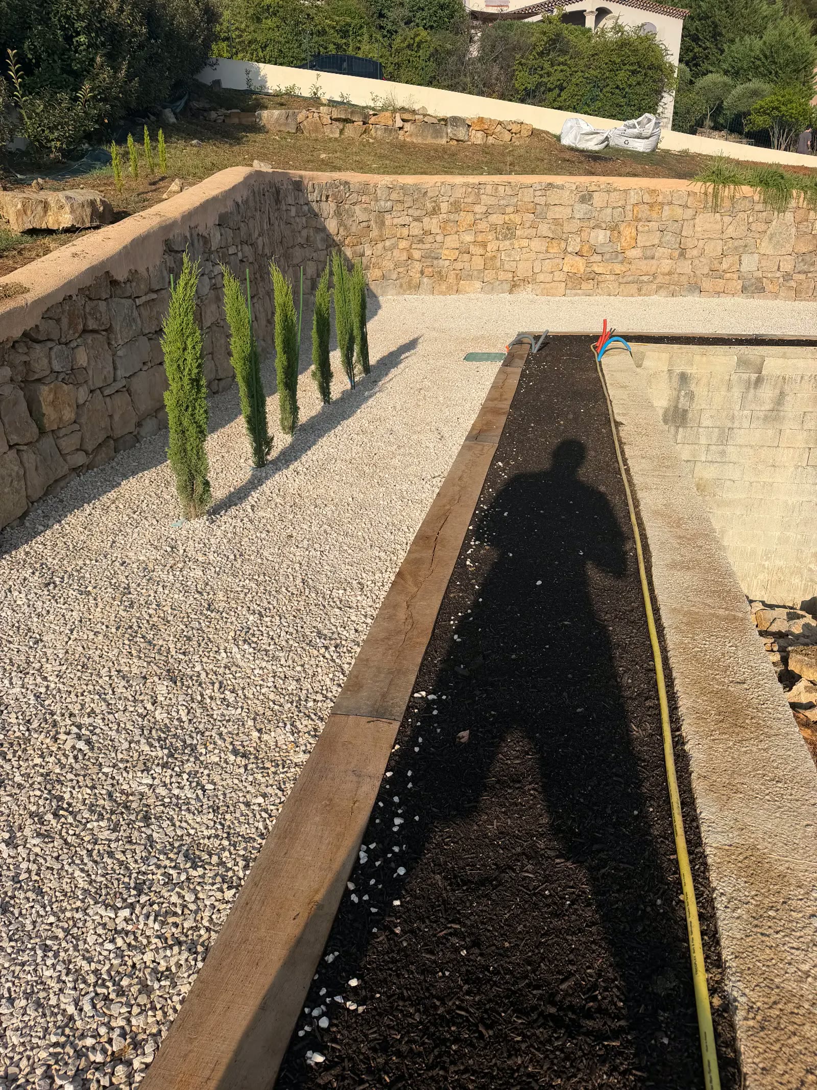 Muret en pierre, allée en gravier blanc et massif paysager avec cyprès